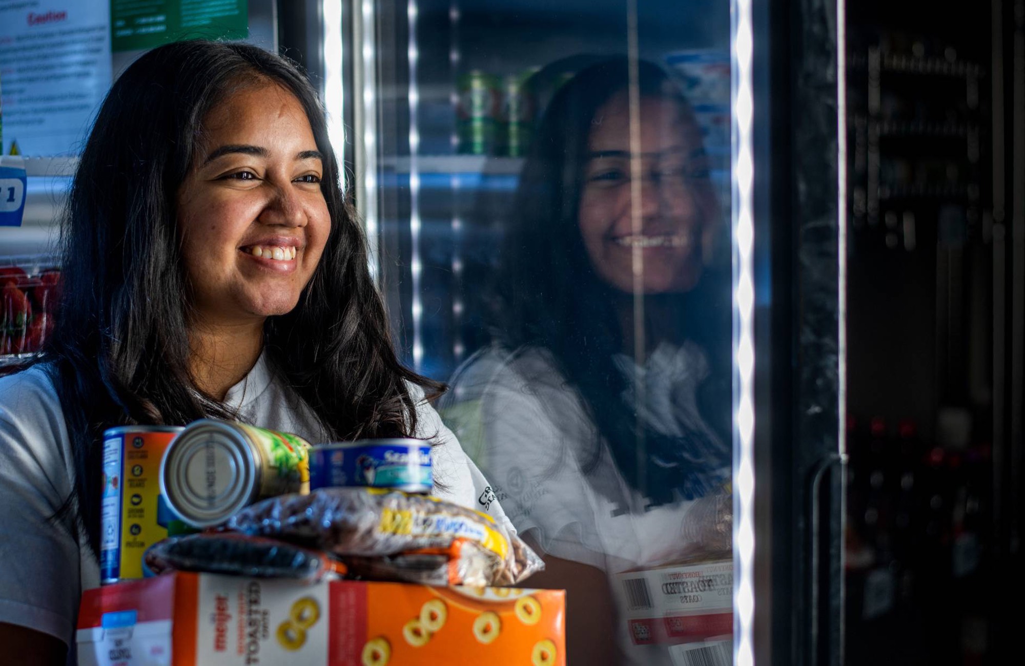 Girl smiling standing by refrigerated food at Replenish